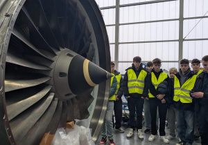 Uczestnicy wizyty studyjnej w hangarze przy silniku oddanym do serwisowania przez LS Technics