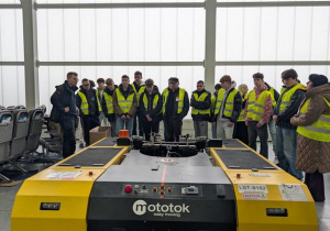 Uczestnicy wizyty studyjnej w hangarze przy urządzeniu służącym do holowania samolotów